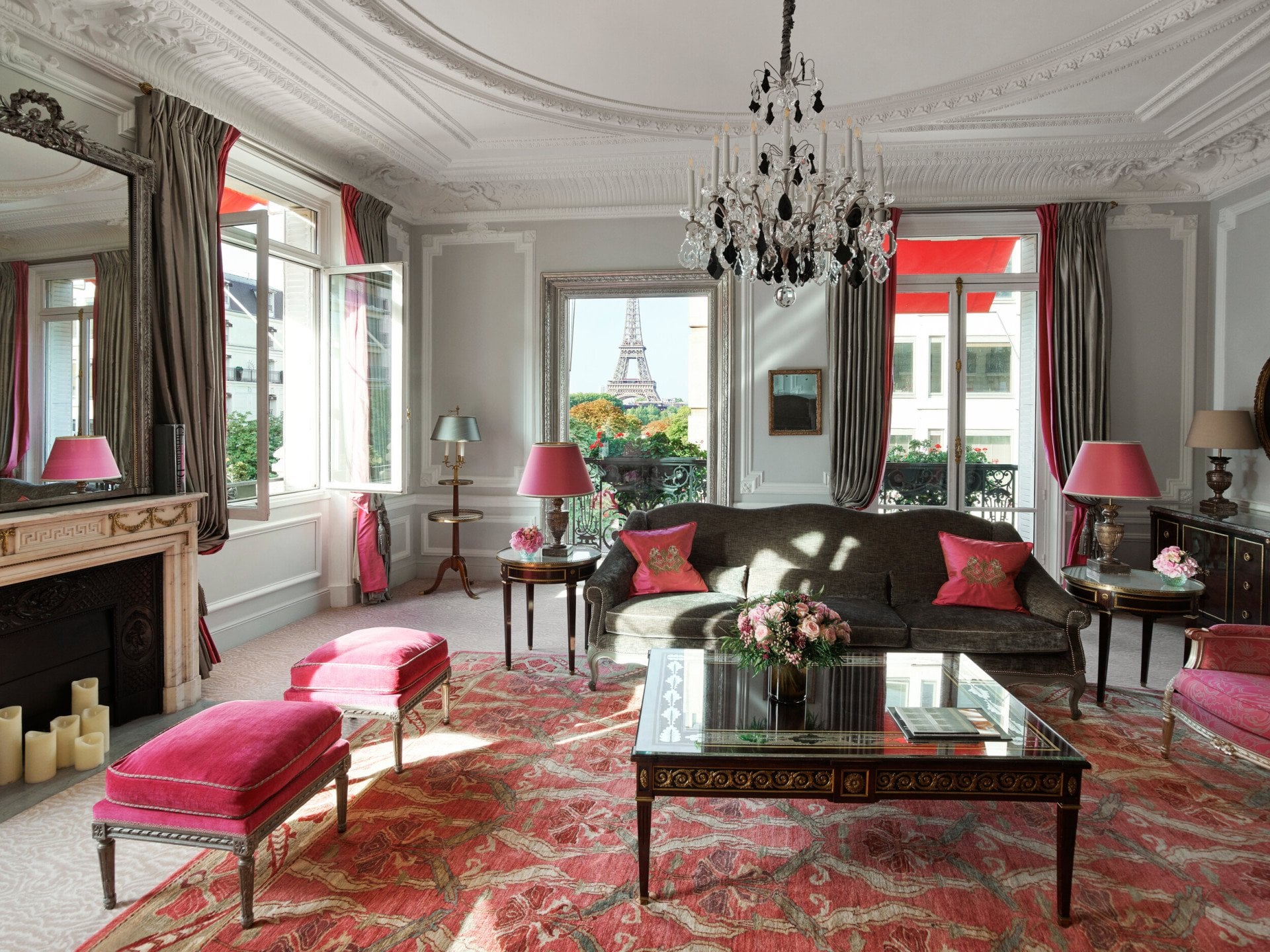 Elegante sala de estar parisiense com decoração vintage, lustre, detalhes em rosa e vista para a Torre Eiffel através das janelas abertas.