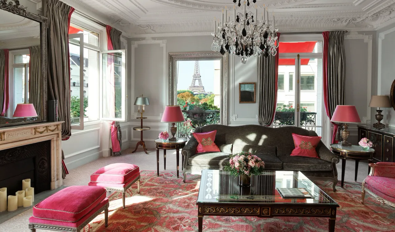 Élégant salon parisien à la décoration vintage, avec lustre, touches de rose et vue sur la tour Eiffel depuis les fenêtres ouvertes.