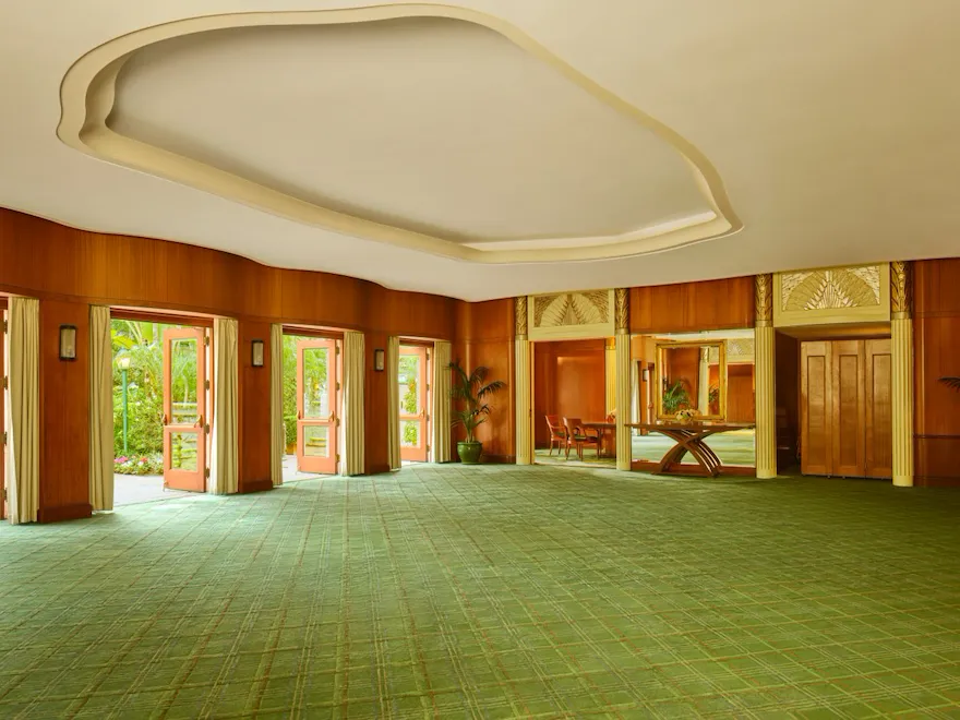 Spacious, empty event hall with large windows, green carpet, and wooden wall panels.