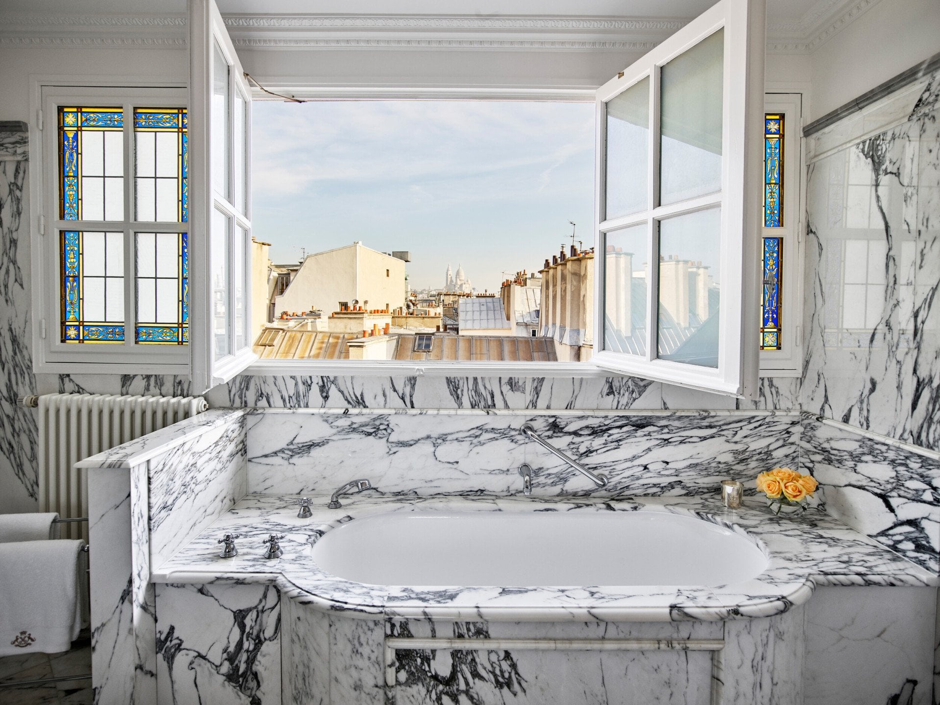 Salle de bains en marbre avec fenêtres ouvertes donnant sur les toits de Paris dans une suite junior exécutive au Meurice, Paris.
