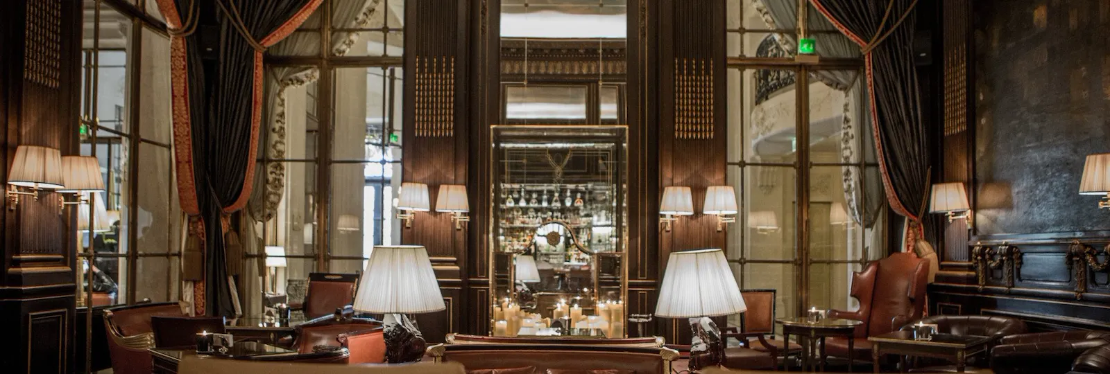 Low tables and chairs, candle and mirrors in the background of the picture reflecting the bar glass shelves, at Le Meurice, Paris.