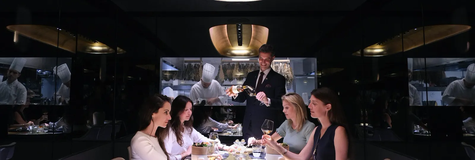 People dine together in a modern, dimly lit restaurant with a server attending to them.