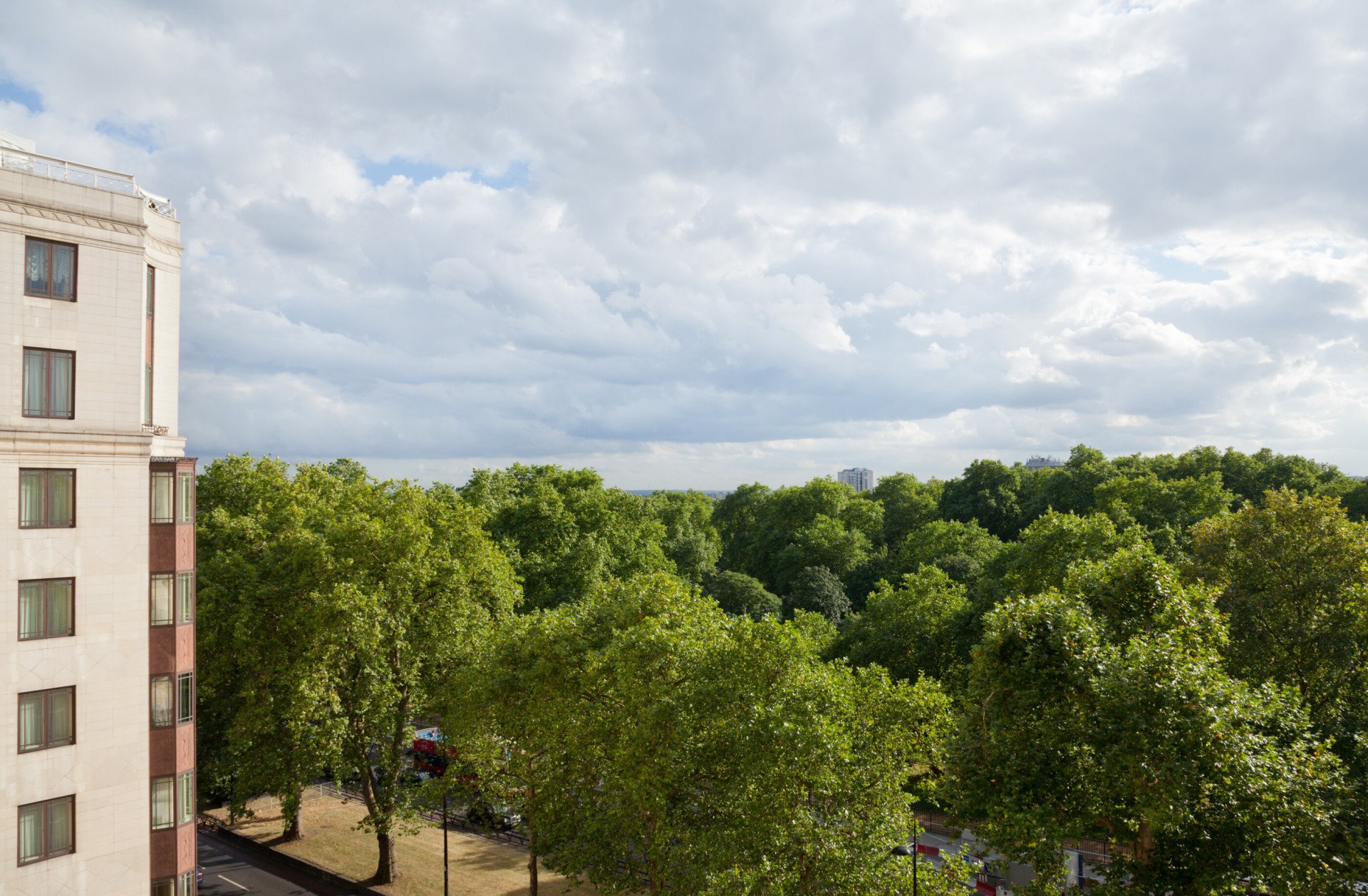 View overlooking Hyde Park from The Dorchester, featuring sweeping greenery, mature trees and a dramatic cloud-filled sky stretching across the horizon.