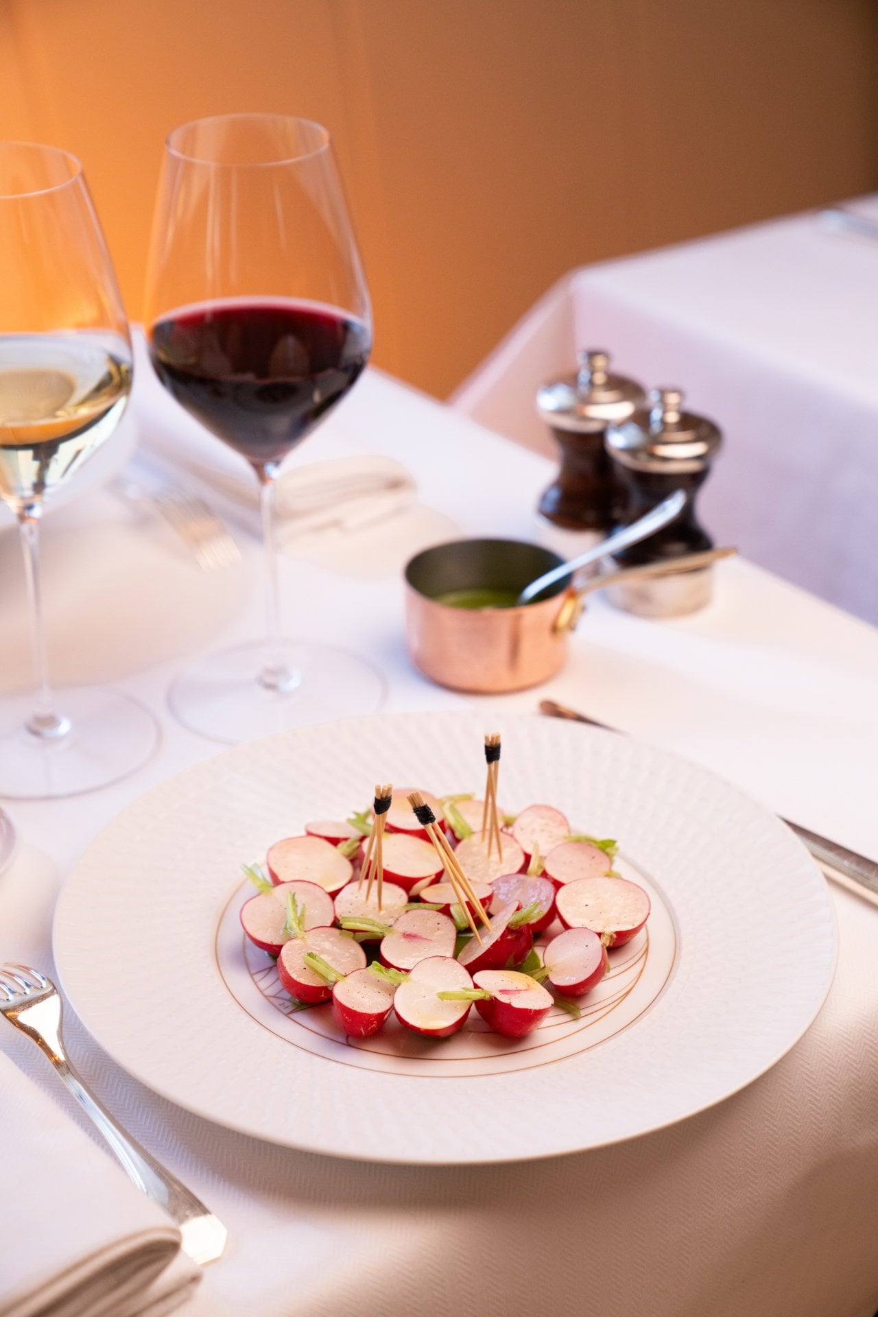 Plate of sliced radishes with toothpicks, wine glasses, and salt and pepper shakers on a white table.