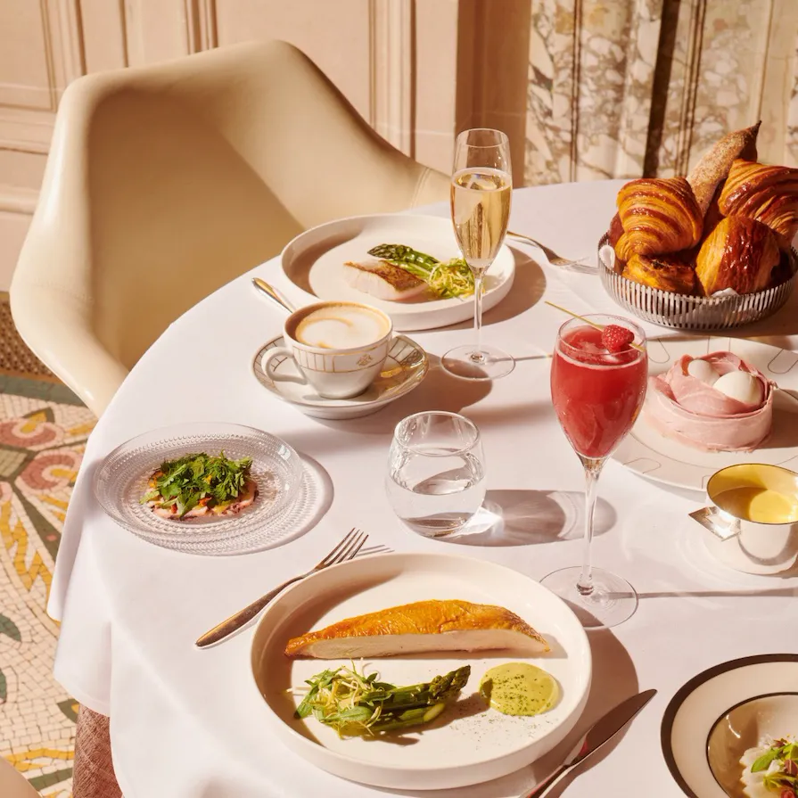Vista superior de uma mesa de brunch com peito de frango com uma taça de champanhe, coquetel e uma xícara de café no Le Meurice, Paris - Coleção Dorchester