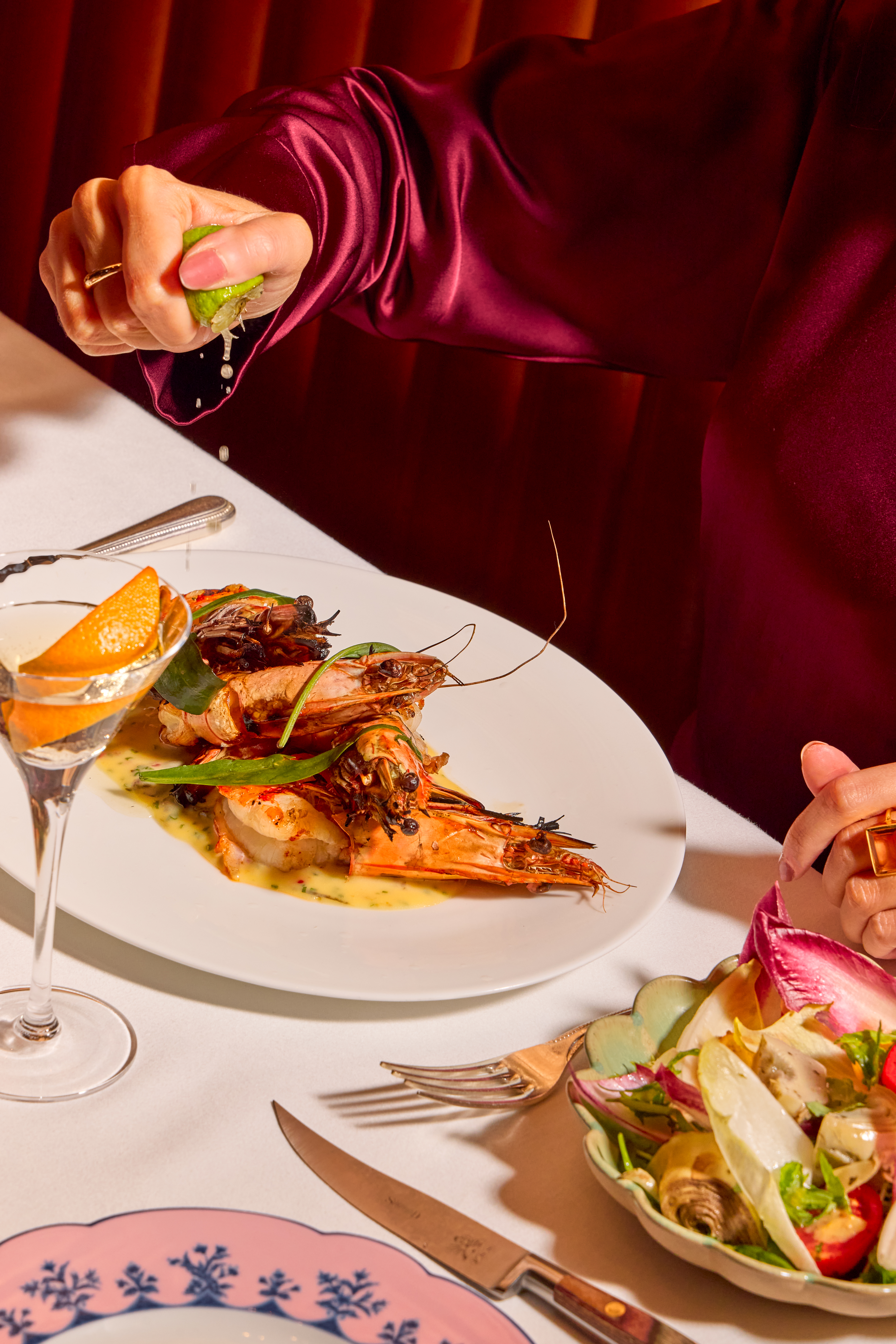 Guest squeezing fresh lime over a prawn dish at The Grill at The Dorchester, with a Martini, side salad and Ginori tableware visible.