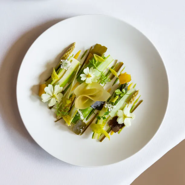 Elegant vegan pasta with herbs and flowers on a white plate, served with a small dish of soya sauce