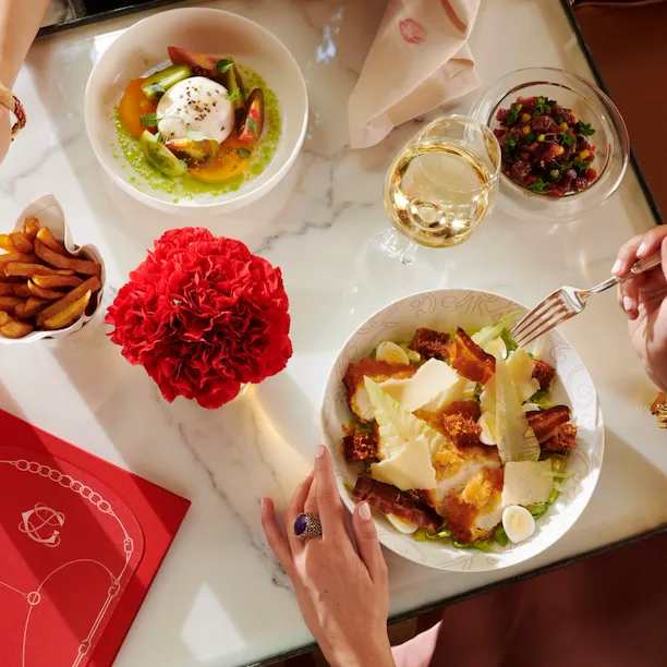 Mulheres almoçando na La Galerie, olhando de suas mãos colhendo batatas fritas e comendo uma salada caesar, McCarthy Salad e vinho branco na mesa, no Hotel Plaza Athénée, Paris