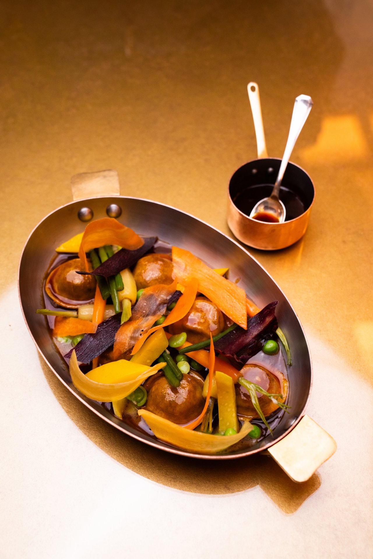 Vegetable dish served in a pan with sauces and utensils on a table, warm and inviting setting