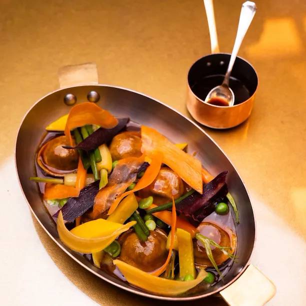 Vegetable dish served in a pan with sauces and utensils on a table, warm and inviting setting