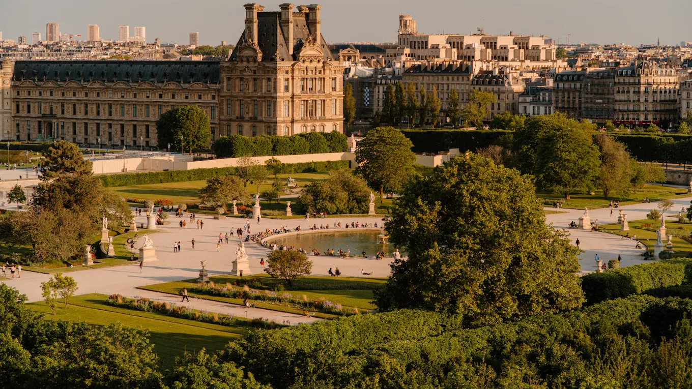 Aerial view of the Tuileries gardens with a smooth yellow light, at sunset. A pond with a fountain and chairs around it is at the center of the picture, at the Tuileries gardens, Paris
