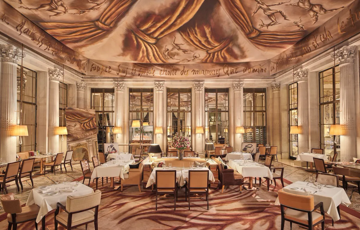 Grande vue sur le restaurant Le Dali avec tous les meubles de salle à manger, le miroir, la moquette et la peinture au plafond, au Meurice, Paris