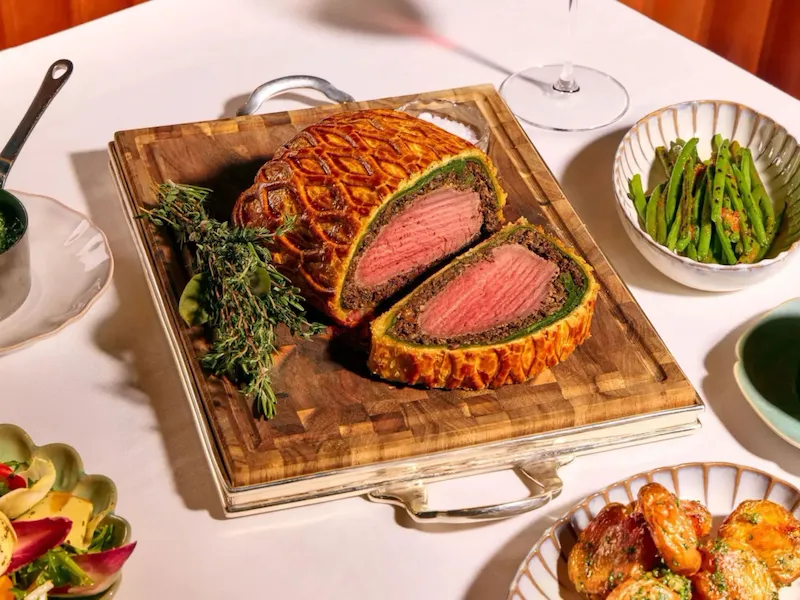 Dining table at The Grill at The Dorchester, showcasing a Beef Wellington sliced to reveal a pink centre, served with asparagus, creamed spinach, roasted potatoes and a fresh seasonal salad.