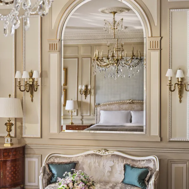 Vista sobre a mesa feita com marchetaria de pedra e um sofá com espelho acima, que reflete o lustre e a cama, no Le Meurice, Paris