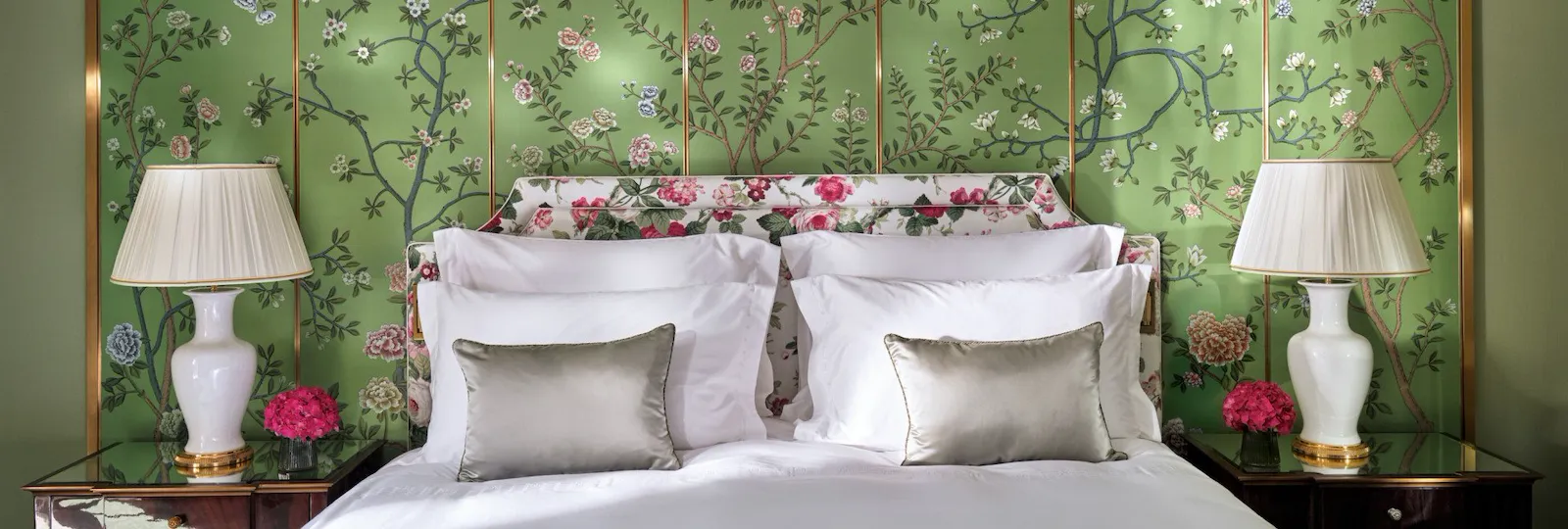 The Belgravia Suite bedroom at The Dorchester, featuring a king-sized bed set against a green wall adorned with an elegant hand-painted floral mural, complemented by bedside lamps and glossy wood furnishings.