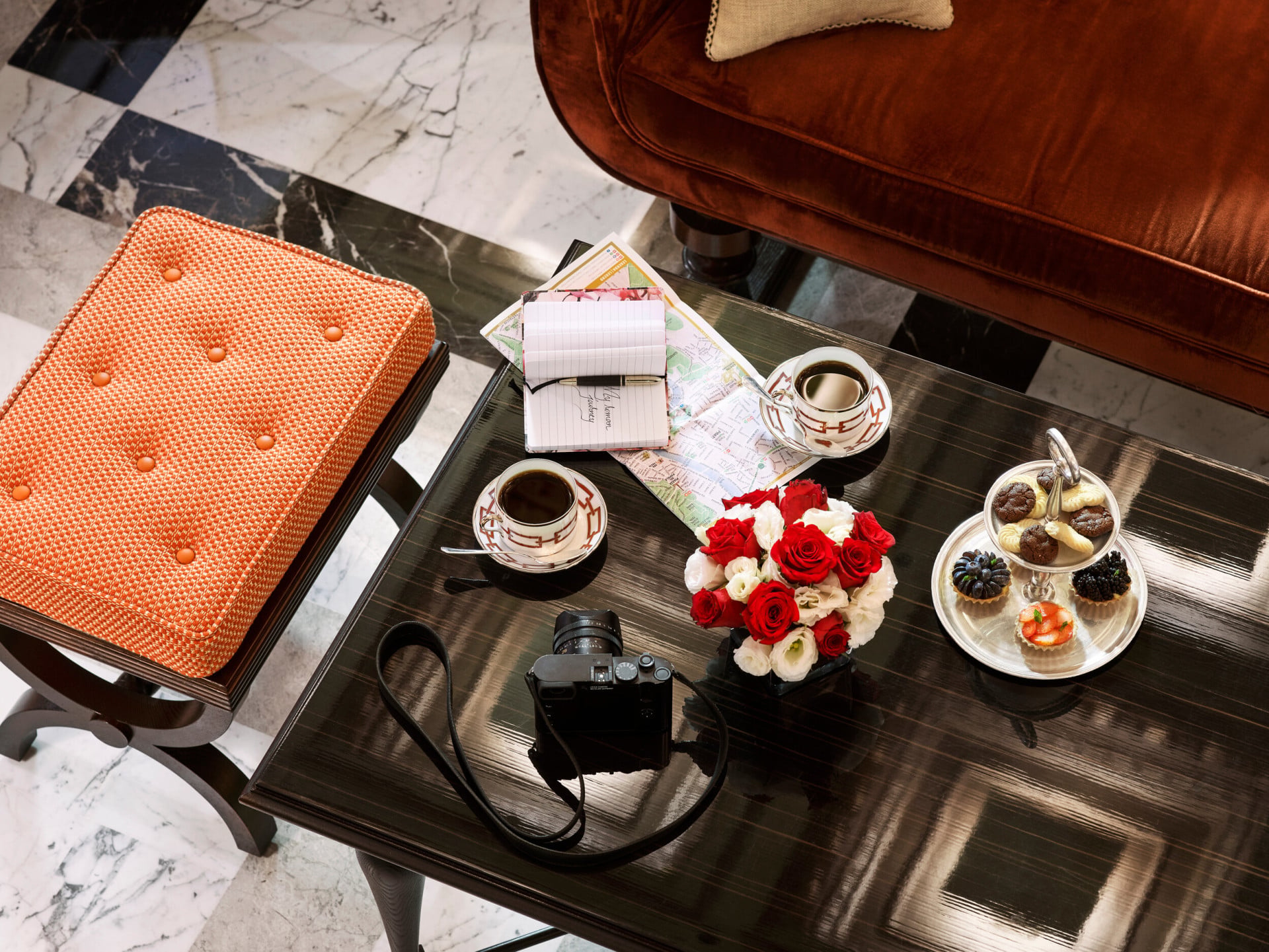 Tavolo da salotto a La Libreria con sopra due tazze di caffè, alzatina di dolci, macchina fotografica, mappa di Roma e taccuino aperto.