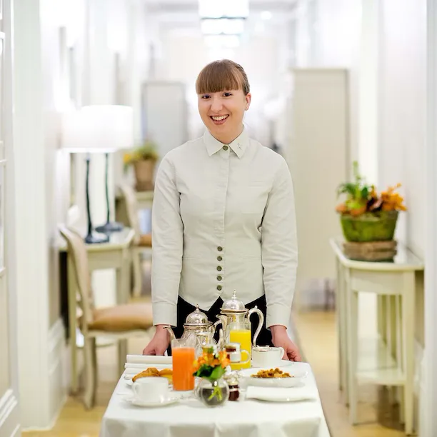 A hospitality staff member standing and smiling, ready to serve in-room dining.