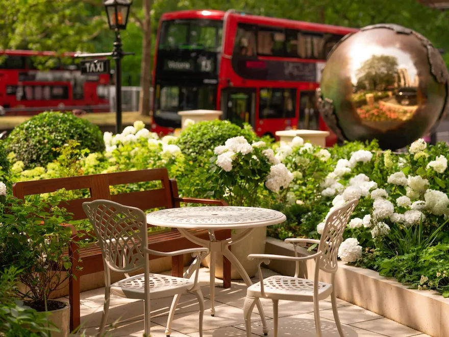The Dorchester’s outdoor garden showcasing the globe sculpture, elegant al fresco seating with views of Hyde Park and a red London bus travelling along Park Lane.