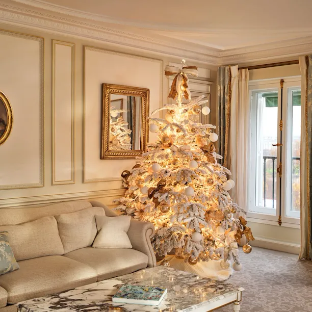 Large view of a Prestige Suite with a table and a couch next to a Christmas Tree with decorations and artificial snow on it, at Le Meurice, Paris