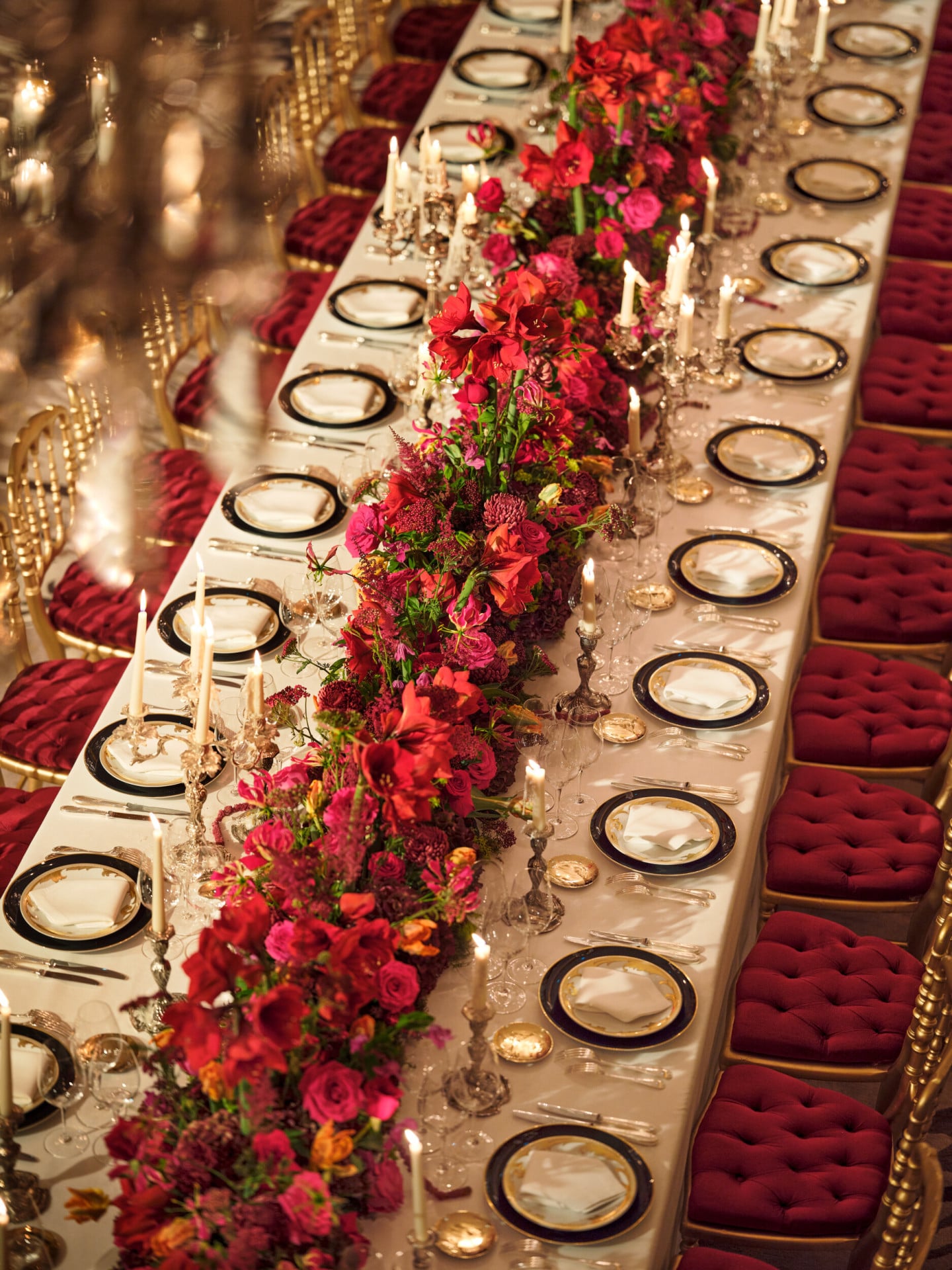 Dinner set up with a long table and red flowers captured in Le Salon Haute Couture, at Hôtel Plaza Athénée, Paris - Dorchester Collection.