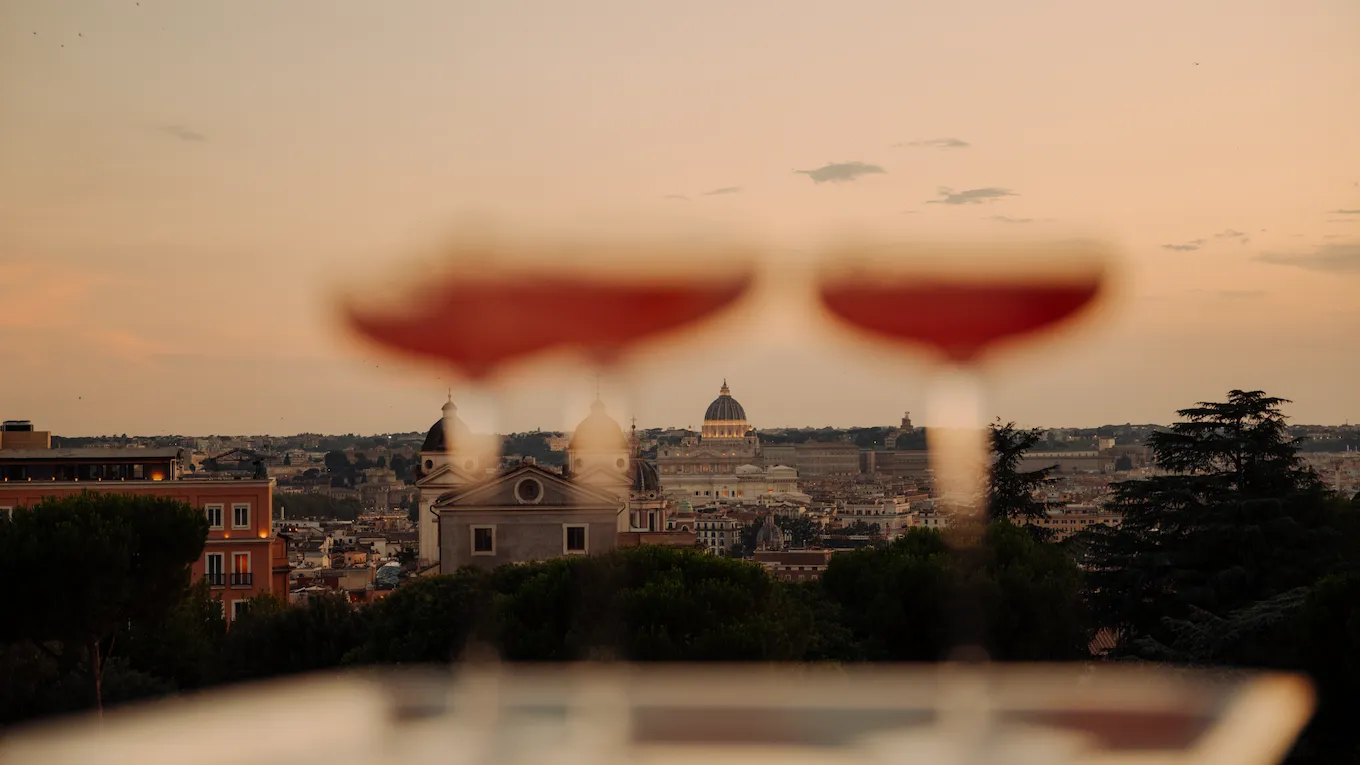 cocktails on a tray held up against a cityscape sunset view with a dome and clouds in the background
