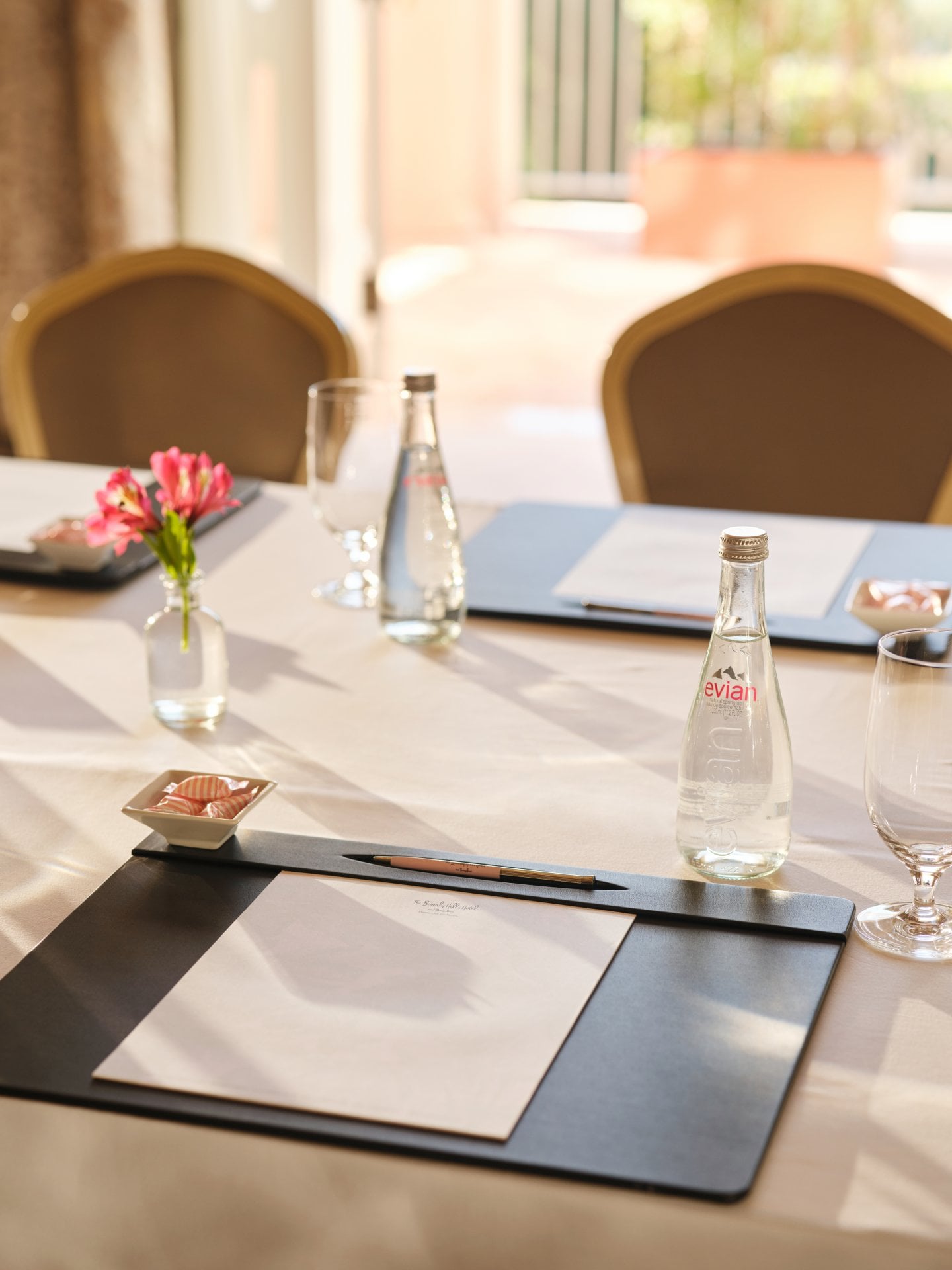 A neatly set table with flowers, water bottles, glasses, and placemats in a bright room