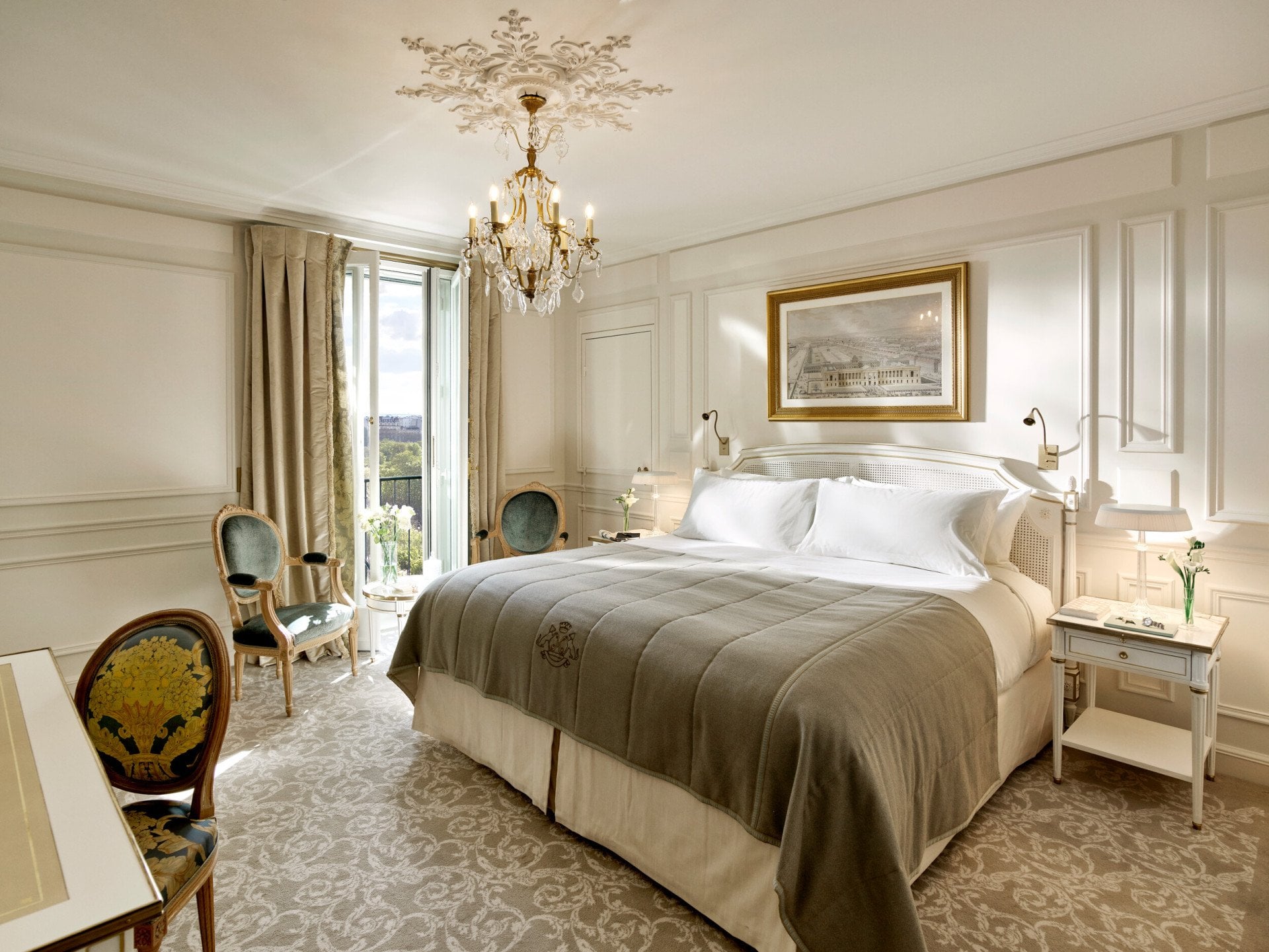 Vista global de um quarto executivo que realça os tons de cinzento claro e creme, bem como a vista sobre os jardins das Tulherias ao fundo. Jóias e livros nas mesas de cabeceiraNo Le Meurice, Paris.