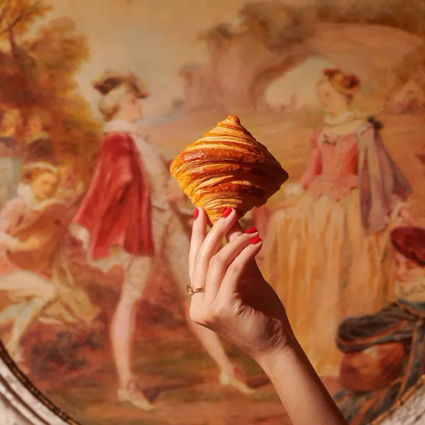 Mão segurando um croissant em frente a uma pintura no Le Meurice, Paris - Coleção Dorchester