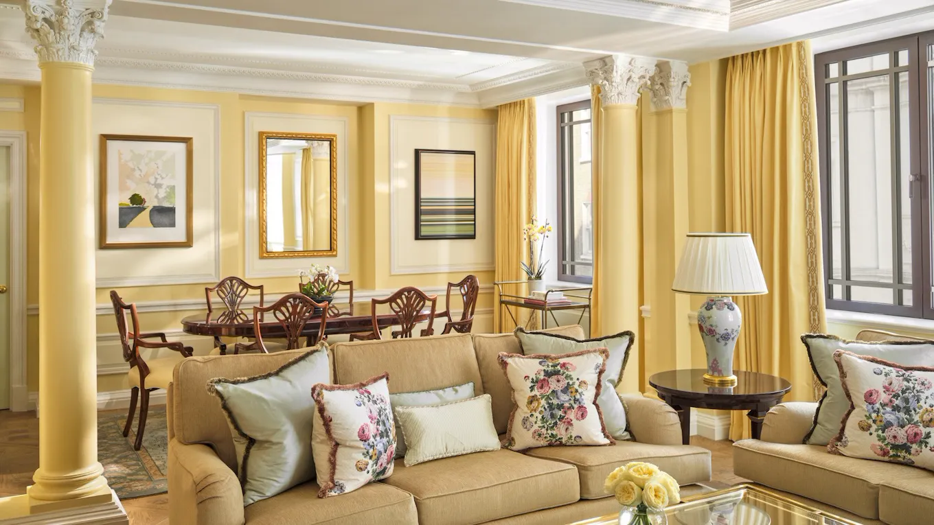 The Dorchester Suite bathed in evening light, showcasing yellow walls, a wooden dining table and an expansive living room designed for comfort and elegance.