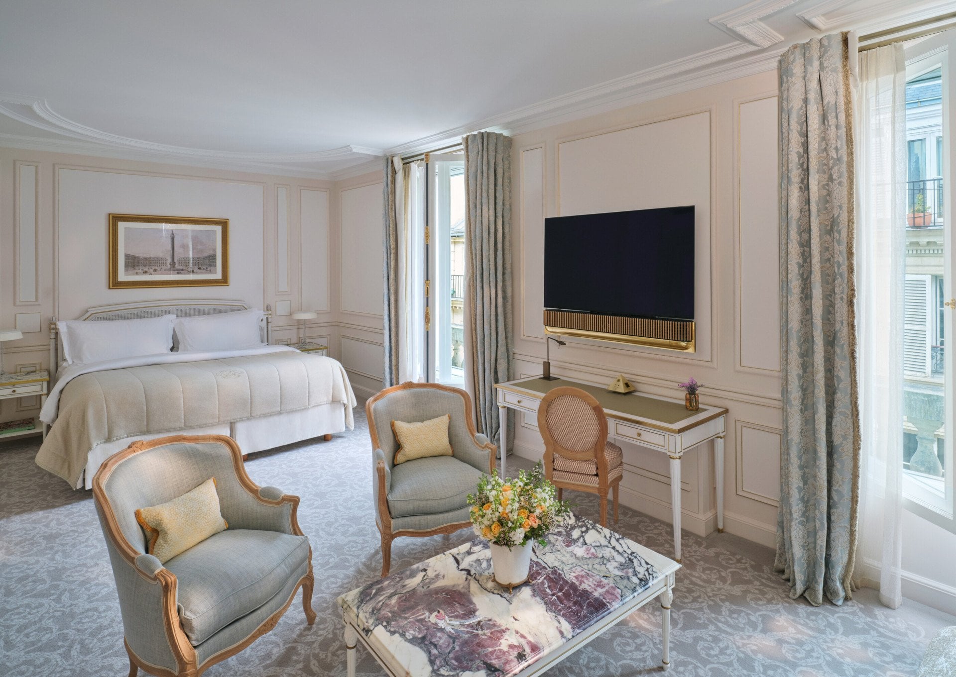 Grande vue d'une Suite Junior Deluxe avec la marqueterie de pierre sur la table et la TV et le Lit en arrière-plan, au Meurice, Paris