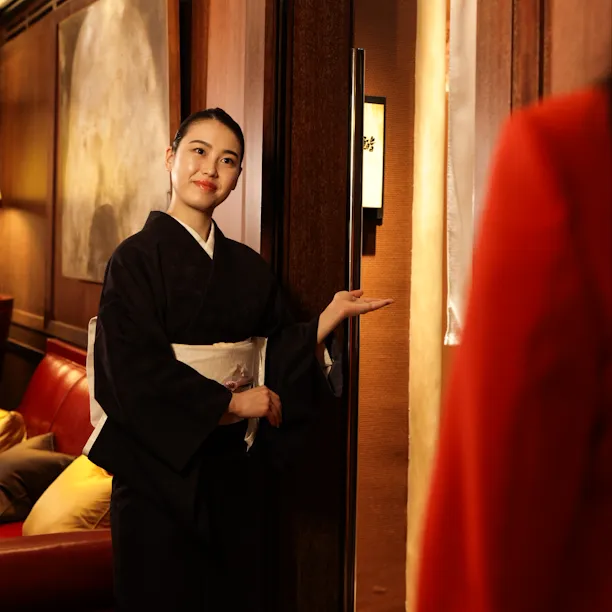 Hostess in traditional black kimono welcoming guests at the entrance of Sushi Kanesaka, 45 Park Lane