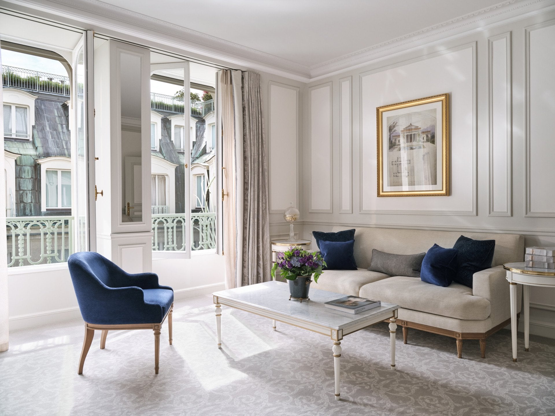 Salon d’une suite de luxe avec une chaise, une peinture au-dessus du canapé et une table avec des fleurs et des livres sur le dessus, au Meurice, Paris