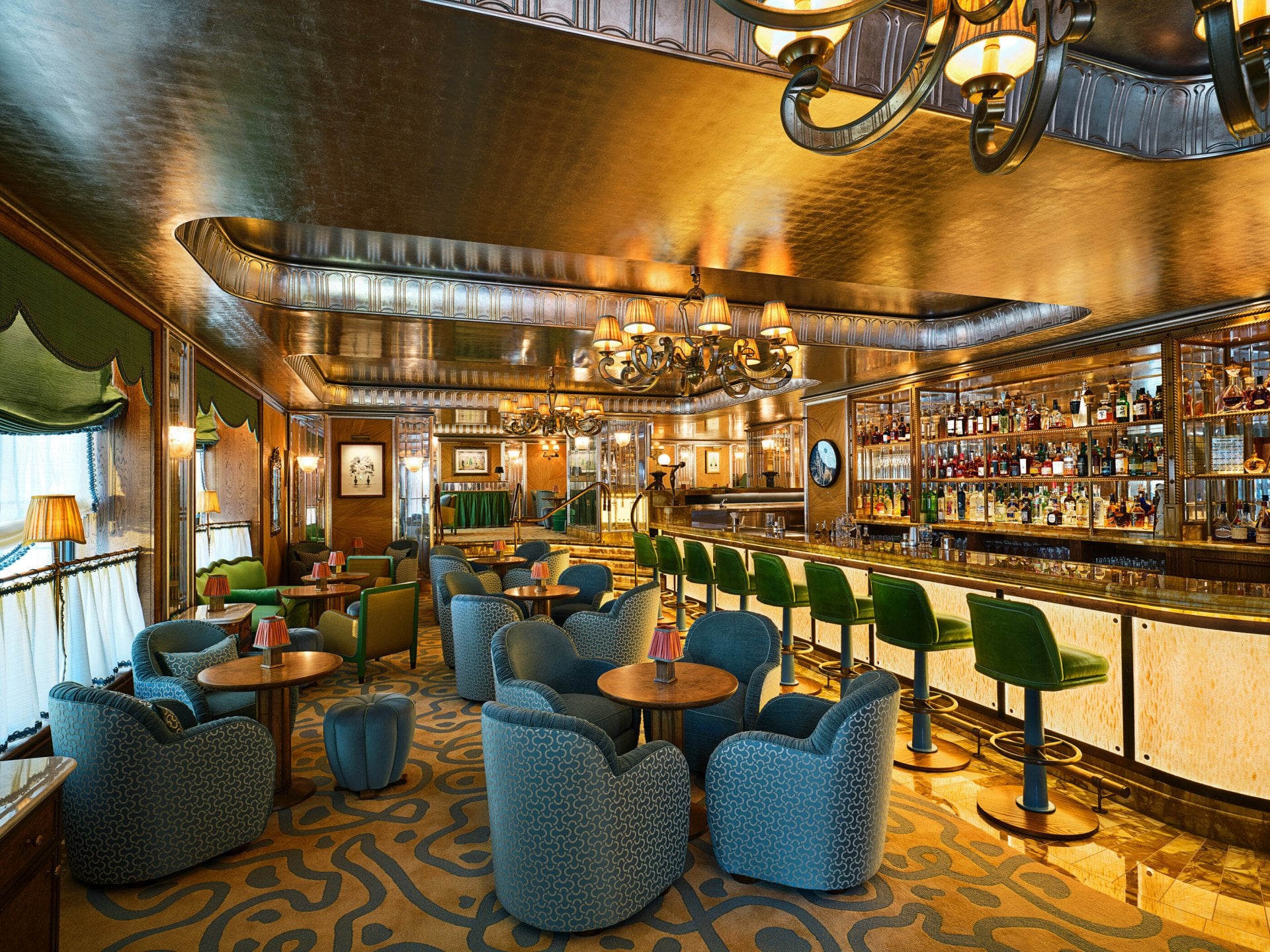 The Vesper Bar at The Dorchester, featuring blue lounge seating, green bar stools and a polished Art Deco bar.